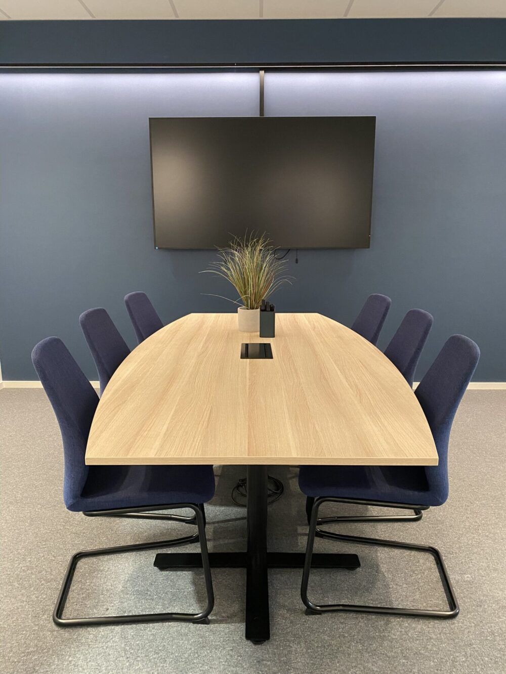 Felles møterom for alle ansatte med skjerm på vegg for presentasjoner og teamsmøter. Den blå fargen fra logoen til Enor går igjen i interiøret.